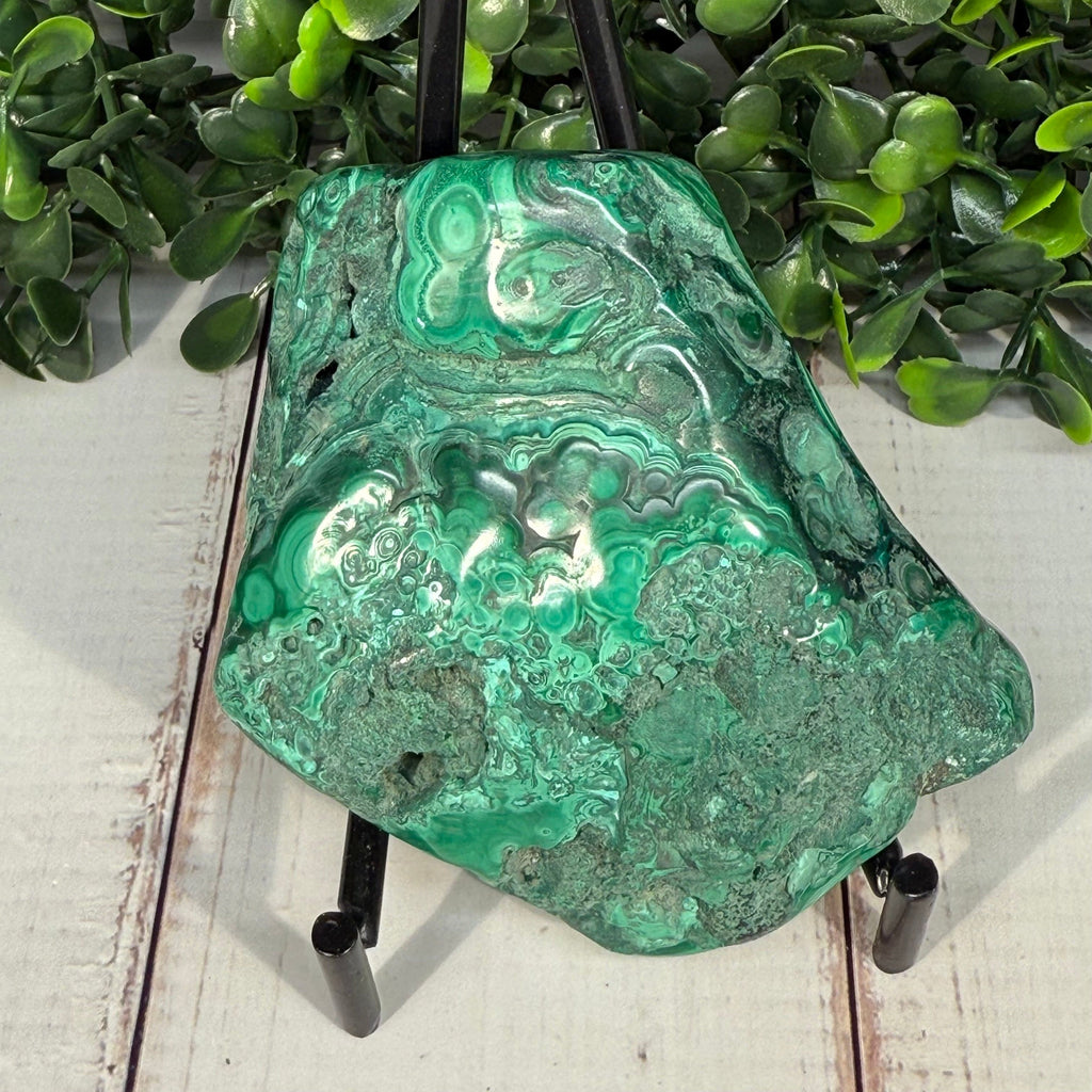 Polished malachite stone showing vivid green orbital banding alongside raw natural surface