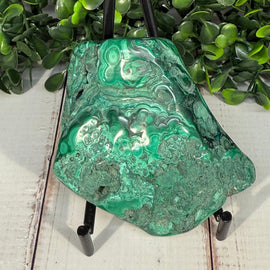 Polished malachite stone showing vivid green orbital banding alongside raw natural surface